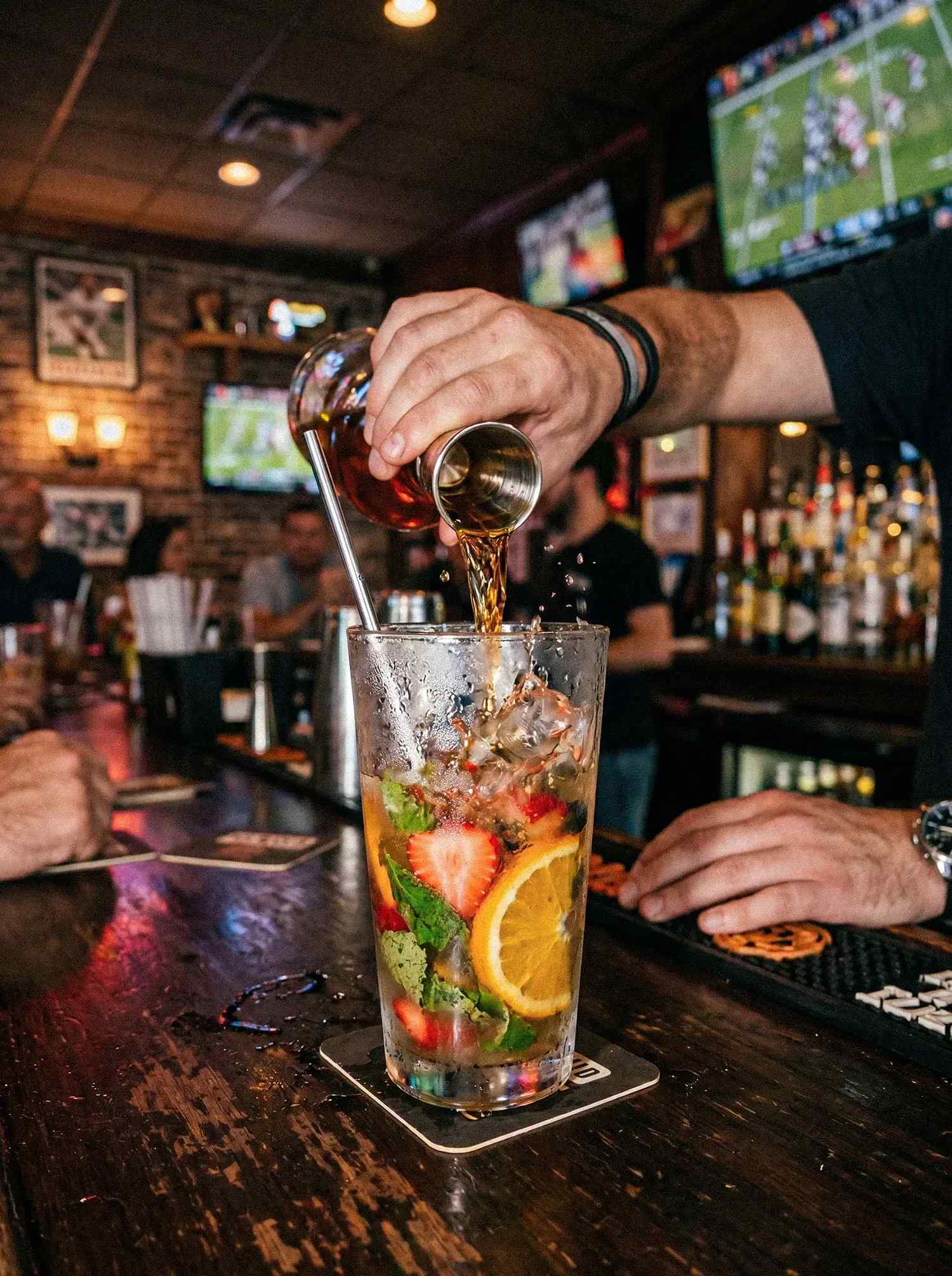 A man mixing a cocktail in a bar with a jigger.